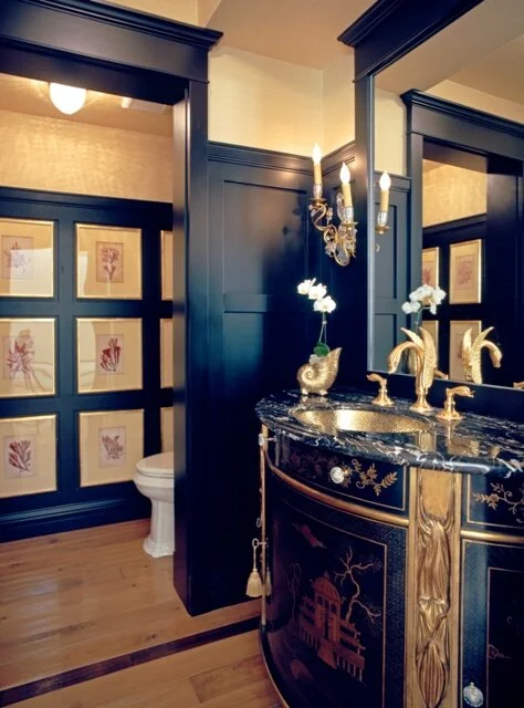 Chinois inspired luxury Powder Bathroom with black painted wood paneling and framed botanical prints on the walls. The gold plated Sherle Wagner faucets and hand painted vanity cabinet show why our Los Angeles Interior Design firm are leaders in the field of home design and decorating.