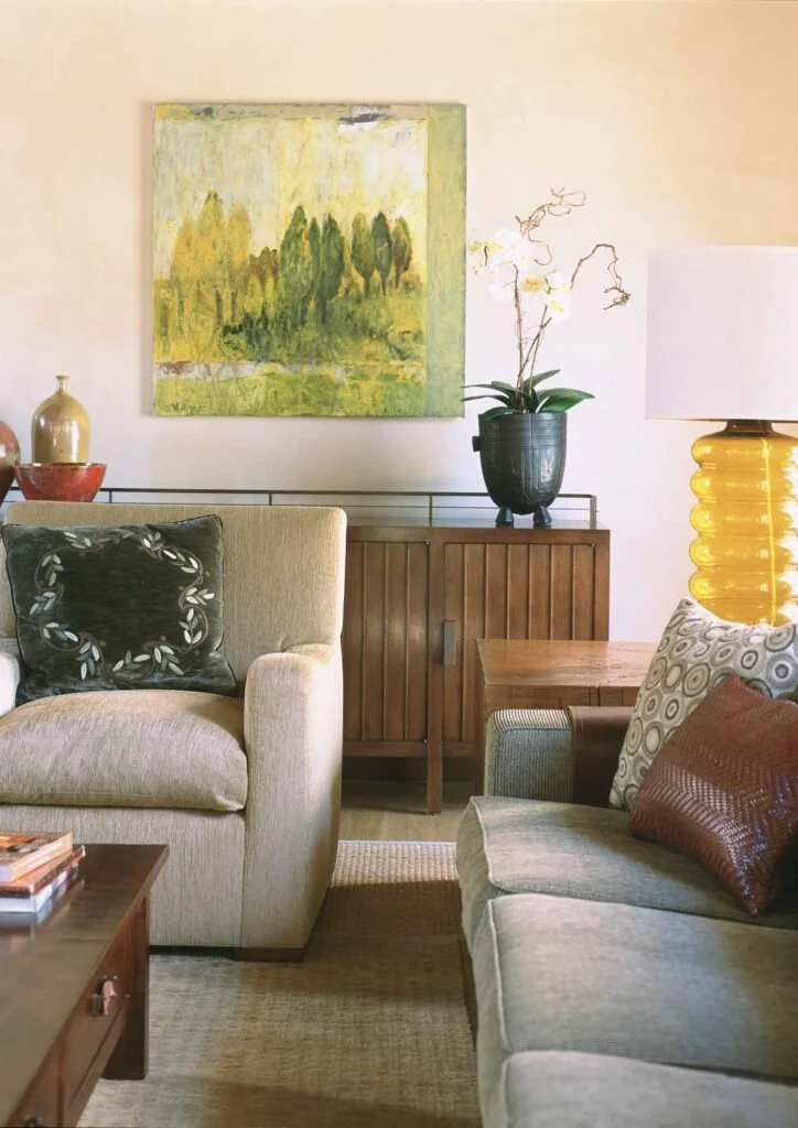 A glimpse at a corner of a living room where two sofas  are corned by an end table.  The sofas are taupe with throw pillows.  A gold accent lamp sits on the table.