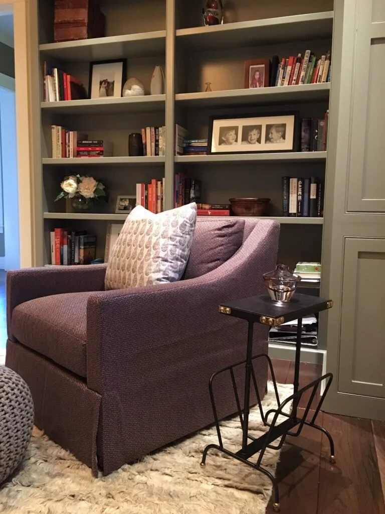 A burgundy upholstered chair with a throw pillow sits in front of a built in bookcase.