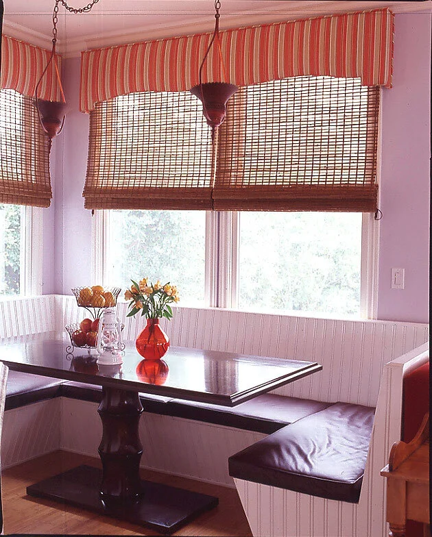 A small dining room with banquette seating net to a window.  The baguette is made of wainscoting with cushions. 