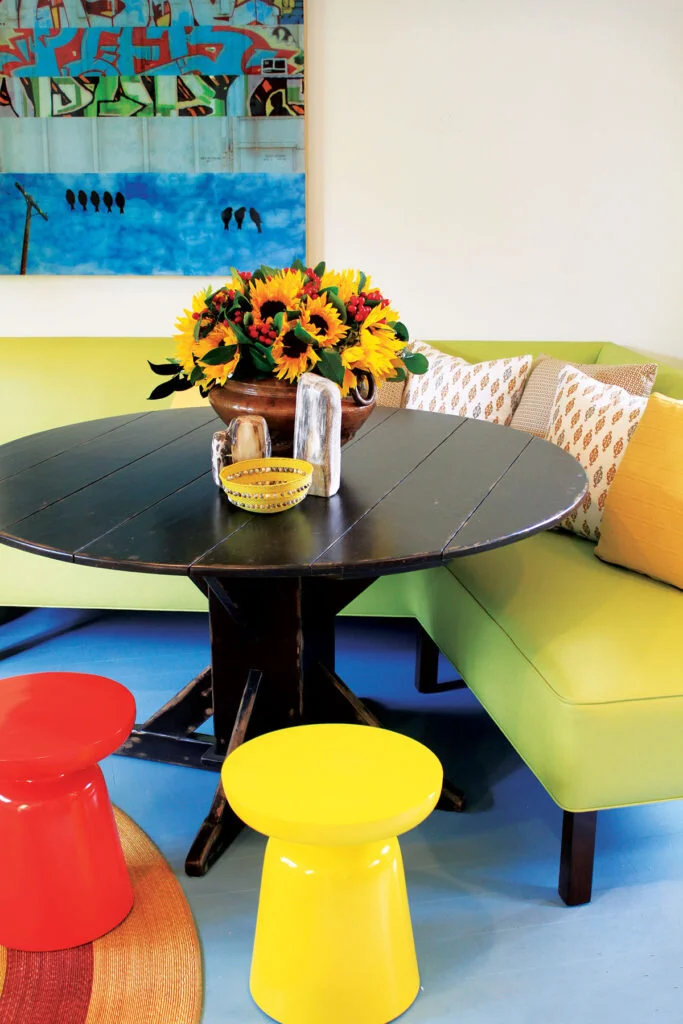 A circular table topped with sunflowers sits nestled into a lime green couch with two brightly colored stools on the other side.