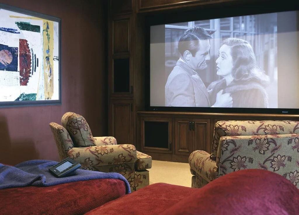 A small in home theater with a bit in cabinet around the screen and comfy chairs and a sofa on multi-levels.