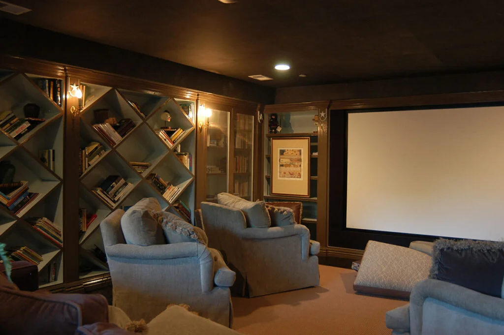 A home theater with bookcases along one wall and cozy chairs in front of a large screen.