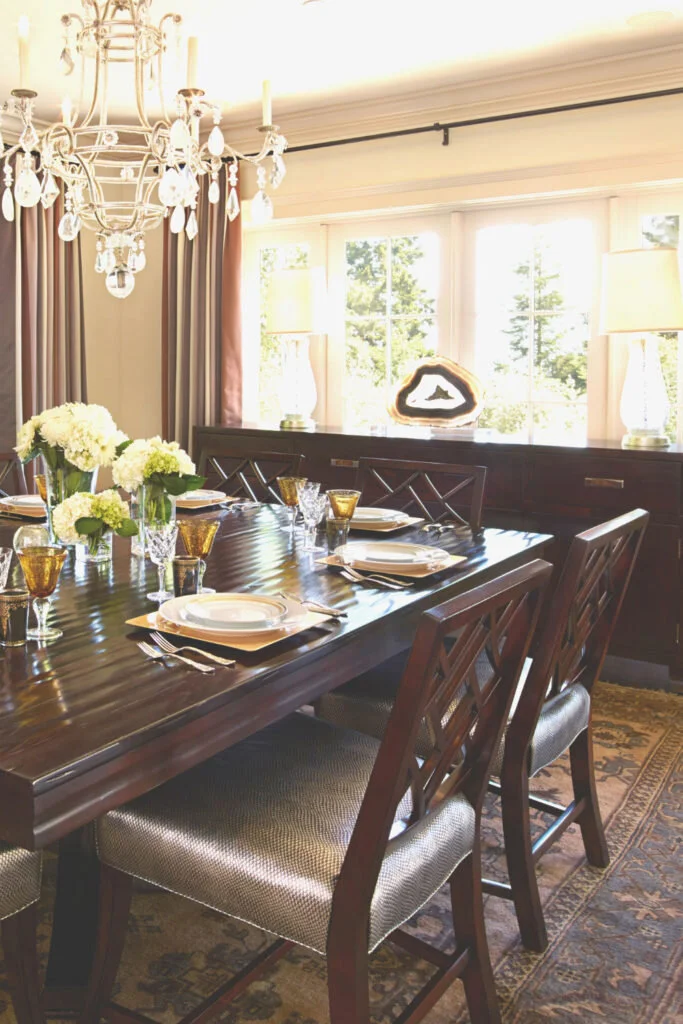 A dining room of dark wood with a chandelier above.  This is a good place to work from home as you have space to spread out and easy access to snacks.
