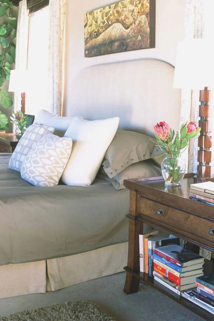 A bedroom in olive green and white.  The bed has a pile of throw pillows.  The bedroom is not a good place to work from home.