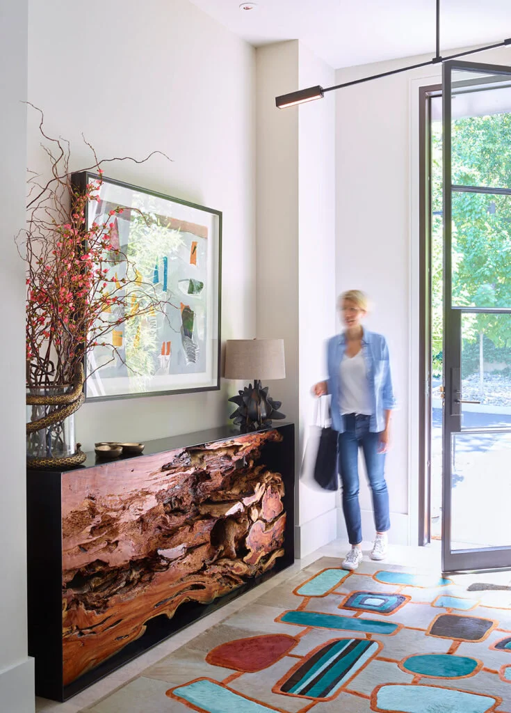 A modern home's entryway in Silicon Valley creates warmth with a steel and teak root console and a multicolored rug.