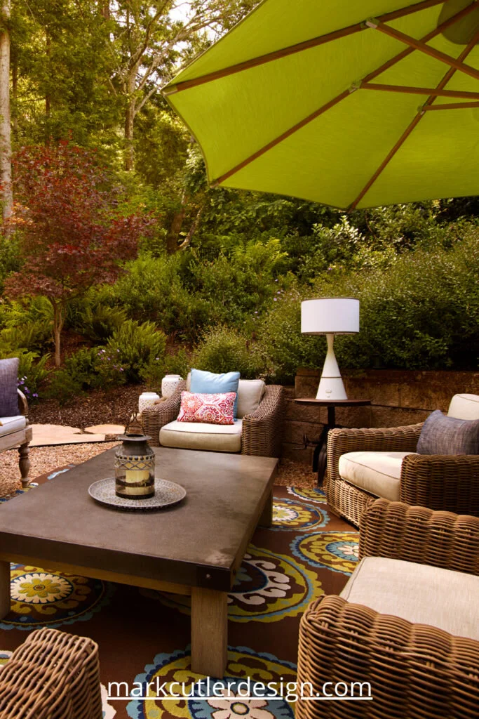This outdoor space in a wooded setting in Northern California has wicker furniture placed around a wooden coffee table.  An outdoor rug anchors the space.