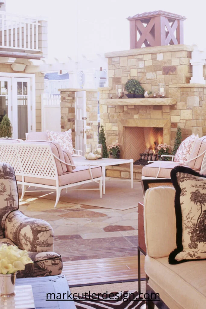 A rubble stone fireplace anchors this outdoor room and creates the perfect focal point, even on a sunny day. Simple white metal furniture with fun red and white stripe upholstery, completes the coastal style feel.