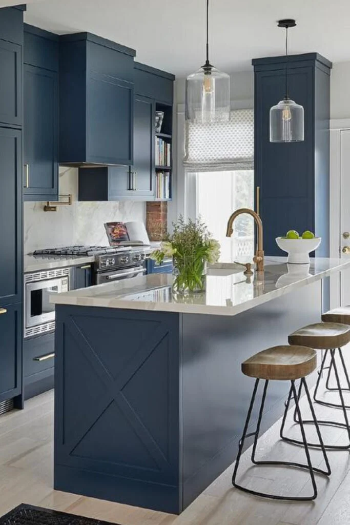 A kitchen with cabinets painted in a medium grayish blue. The countertops are white marble and natural wood and metal stools sit at the bar.