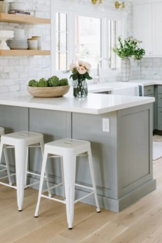 A kitchen with cabinets painted in a soft grey color with white stools and a white countertop.