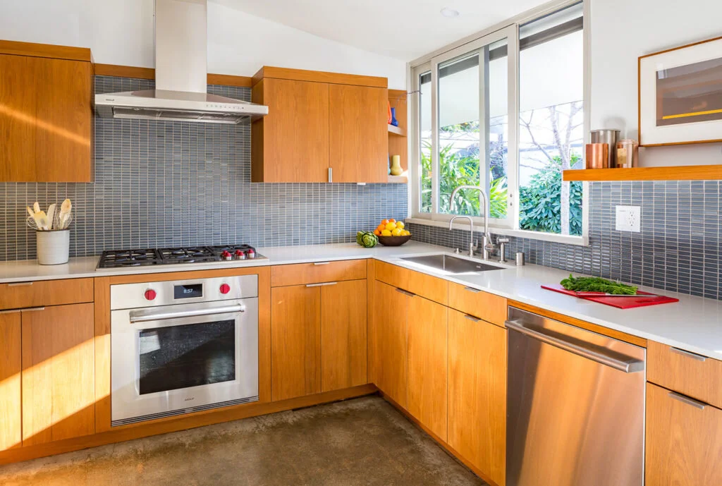 A mid-century modern kitchen with teak cabinets and stainless steel appliances designed by Mark Cutler Design.