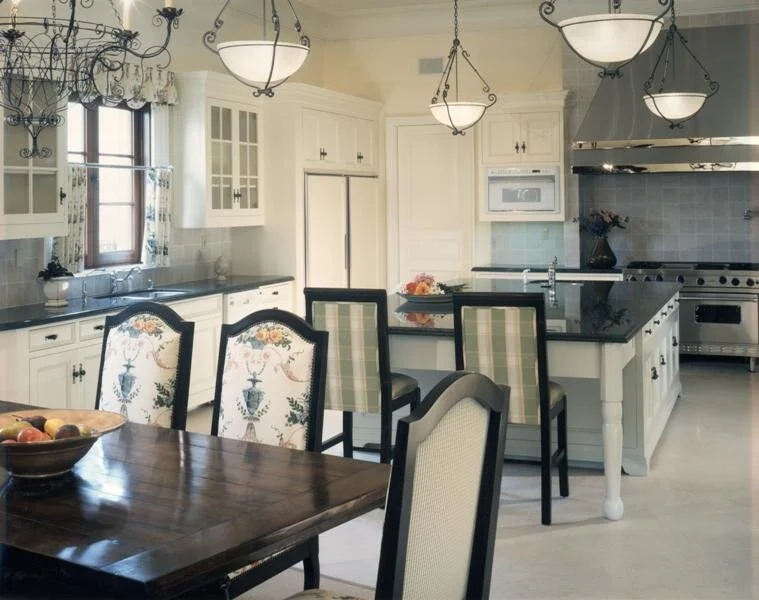 A more traditional white kitchen with black countertops and a farmhouse table. Designed by Mark Cutler Design.