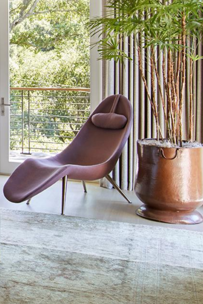 A dusty pink chaise lounge beside a large barrel planter.  A chaise is timeless whether it is contemporary, like the one pictured, or more traditional.