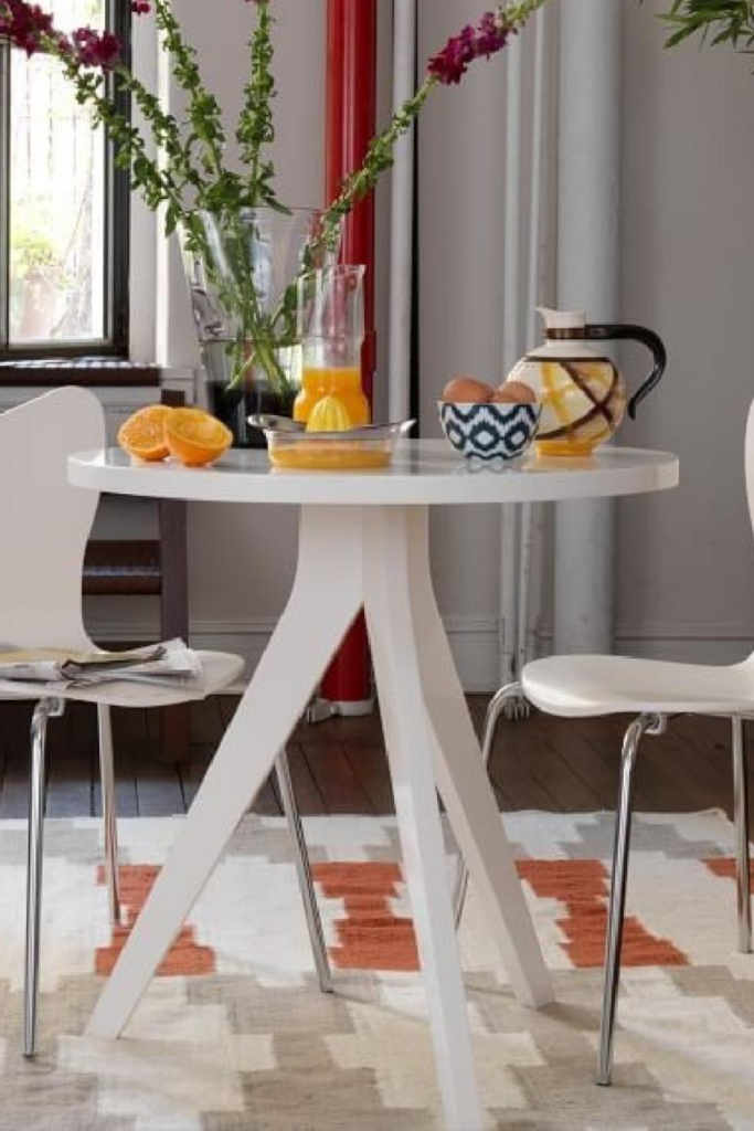 A white tripod table is flanked by two chairs.  It is the perfect statement of minimalism and timeless.