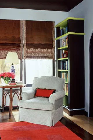 A white comfortable chair with a red pillow sits in front of a bookcase that is painted black with lime green accents.  A holiday refresh can be achieved by painting a room.