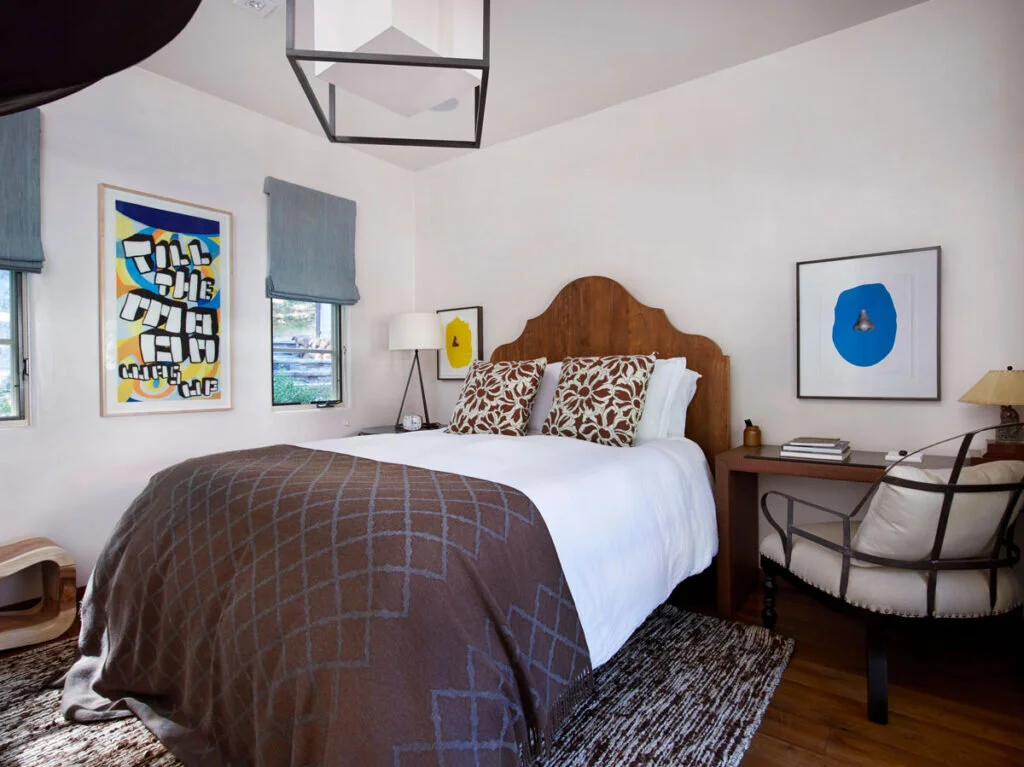 A bedroom that is comfortable and has function. The bed is flanked by a sidetable/desk with a chair beside it.