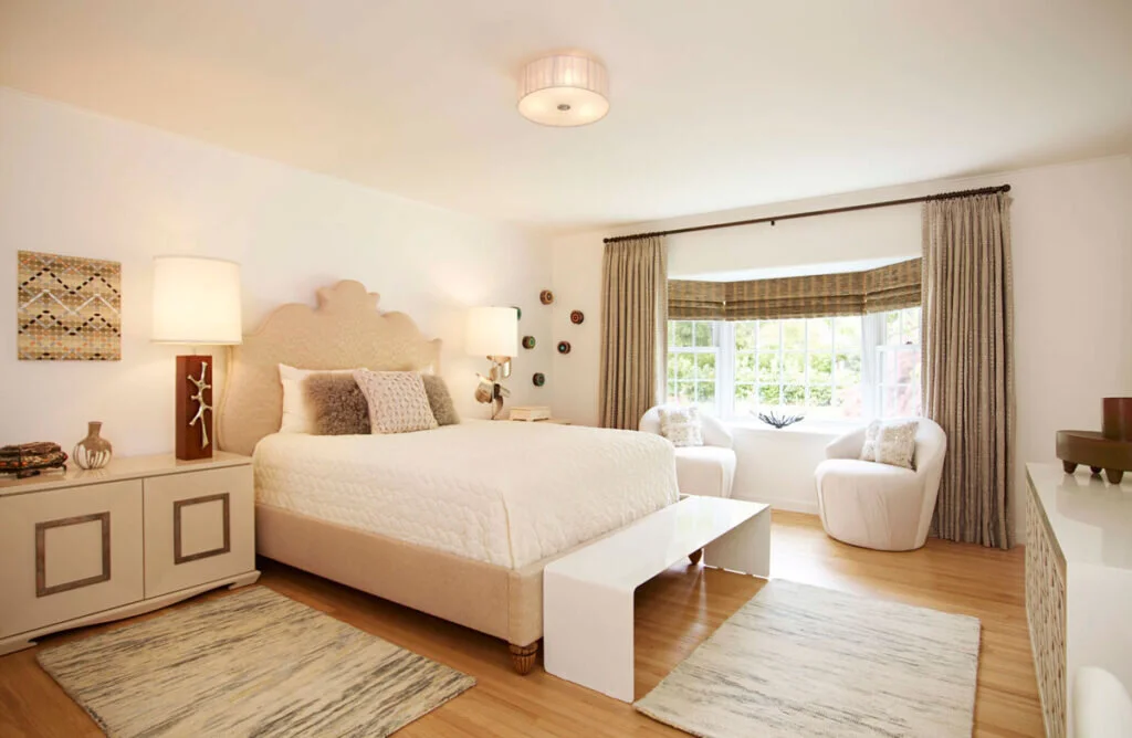 A neutral bedroom with a large bay window. The windows have bamboo shades and curtains.