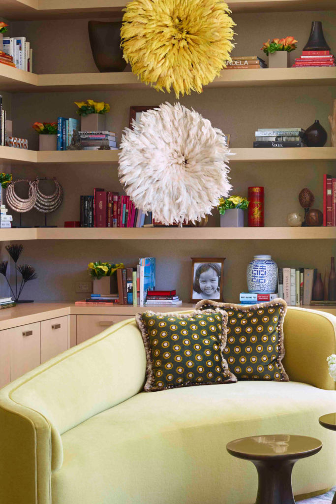 Photo of a love seat in front a built in bookshelf. The shelf has two large flowers hanging as art.