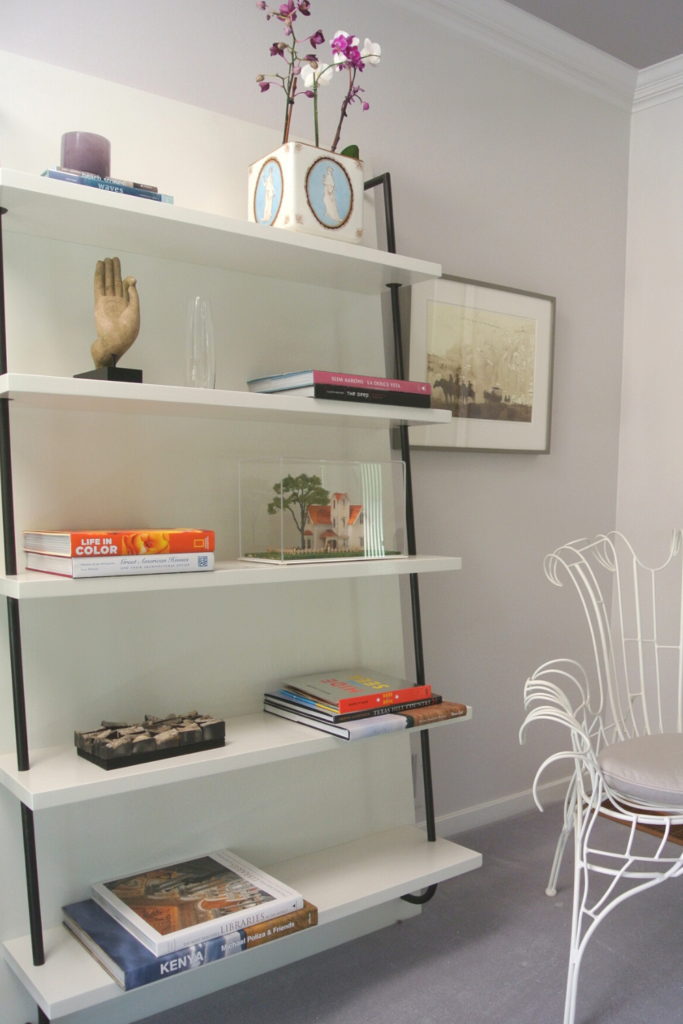 A modern open bookshelf displays small stacks of books and artwork.